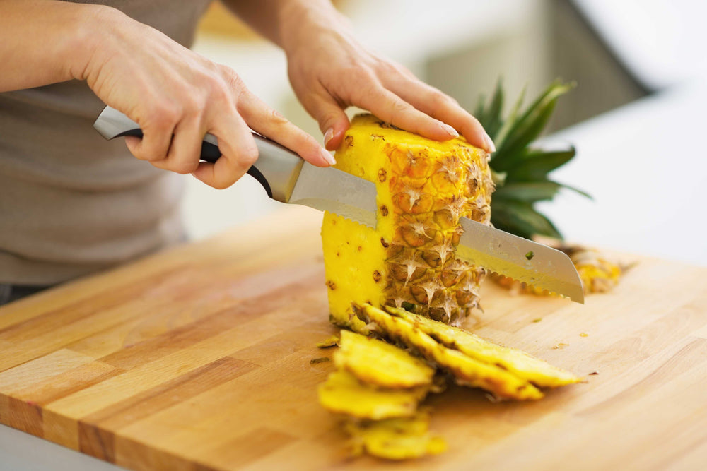 A person slicing the skin off a pineapple A
